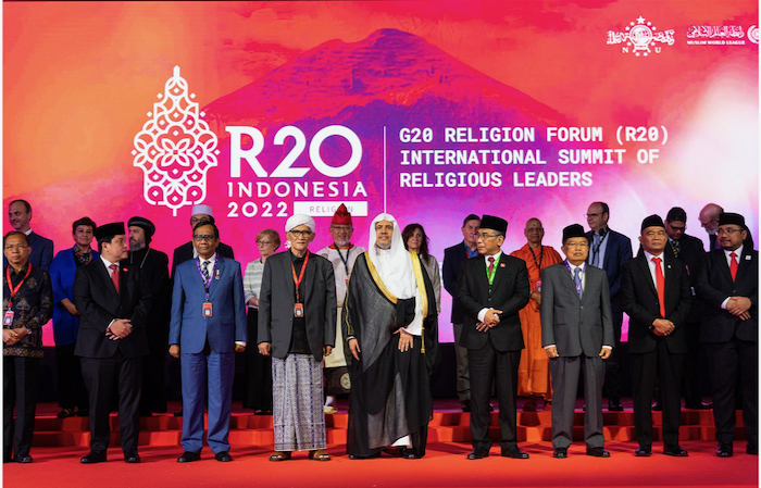 Um grupo diversificado de líderes religiosos em frente a um cenário colorido com as palavras "R20 Indonésia 2022 | Fórum Religioso do G20 (R20) Cimeira Internacional de Líderes Religiosos"
