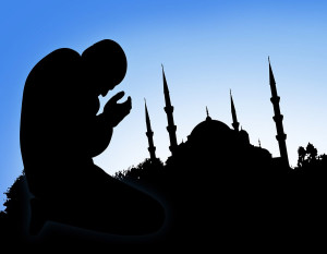 Silhouette of a man bowing his head in front of a mosque
