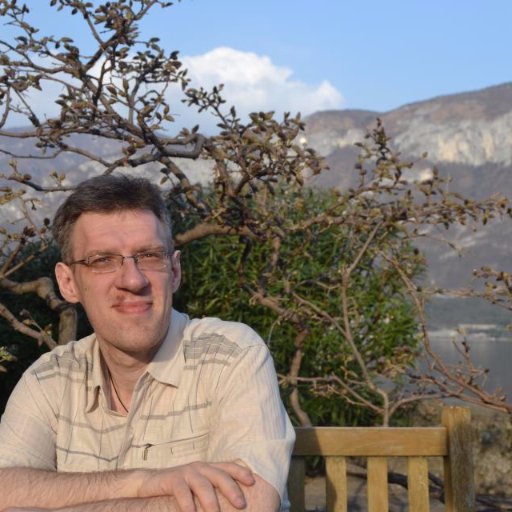 Journalist Sasa Milosevic smiling at the camera in the foreground with trees and mountains in the background