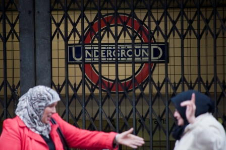 Zwei Frauen mit Kopfbedeckung unterhalten sich vor einem bebenden Eingang der Londoner U-Bahn